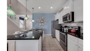A modern kitchen with white cabinets, a black countertop, and stainless steel appliances. - Spacious 7 BR Villa with Pool, Spa, Themed Rooms (Kissimmee)