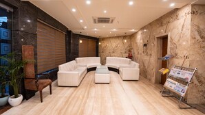 A modern lobby with a seating area, marble walls, and a magazine rack. - JS Residency (Varanasi)