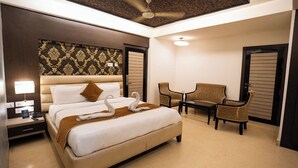 A hotel room with a large bed, a desk, two chairs, a ceiling fan, and a patterned wallpaper. - JS Residency (Varanasi)