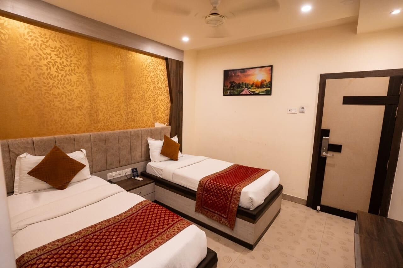 A hotel room with two beds, a nightstand, a ceiling fan, a painting on the wall, and a door.