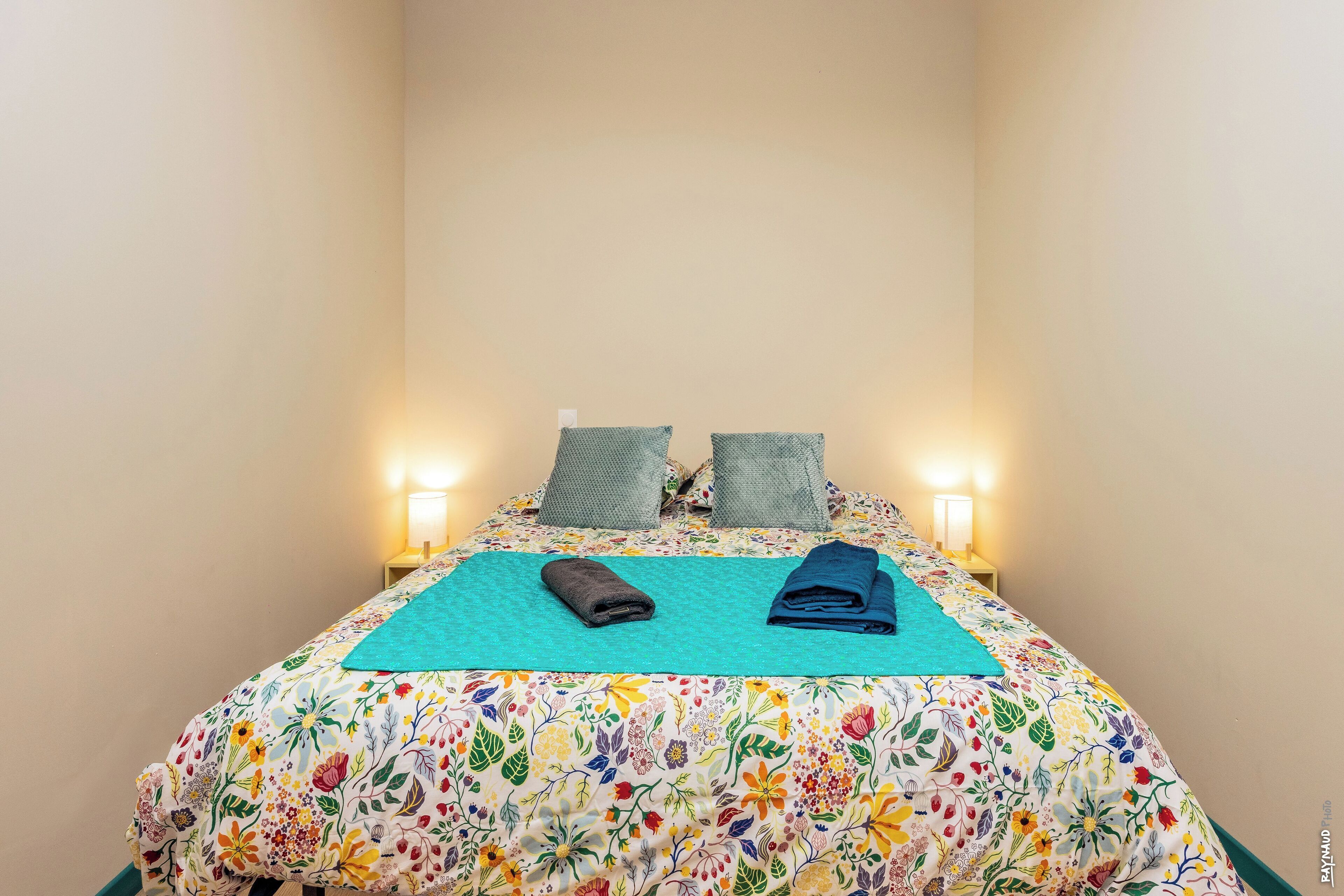 Un letto con biancheria da letto a motivi floreali, due cuscini e due asciugamani piegati.