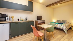 Una cucina compatta con forno a microonde, tostapane e lavandino. C'è un tavolo di legno con due sedie, un letto con copripiumino floreale e un piccolo armadietto di legno.