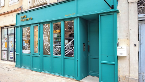 Una vetrina color petrolio con il nome "Café Mercerie" e un cartello che riporta "MOHA".