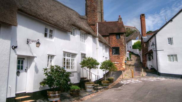 A narrow street lined with traditional white buildings with thatched roofs and stone chimneys.