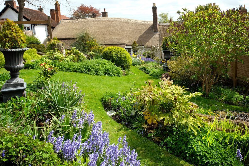 Un jardín con diversas plantas y una casa con techo de paja.