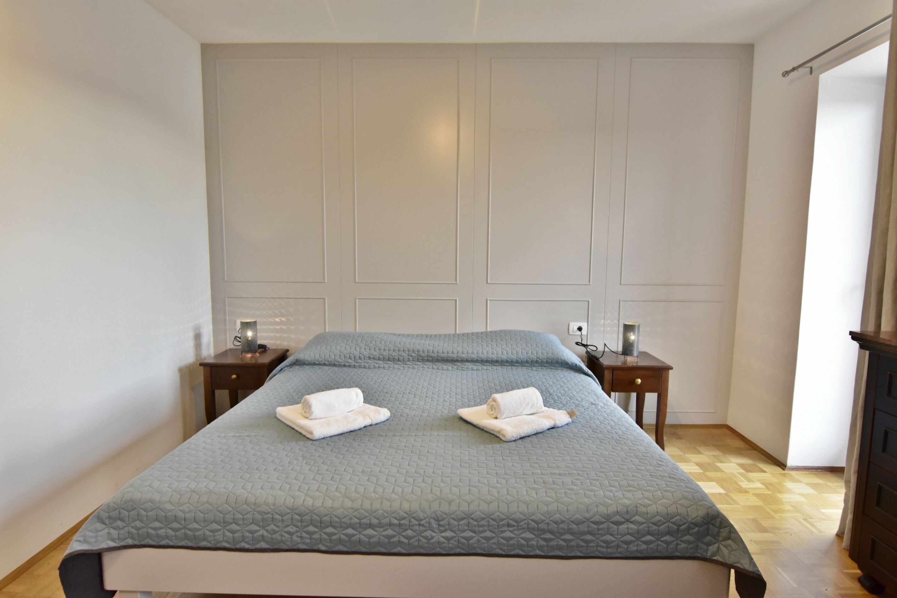 Un lit bien fait, recouvert d’une courtepointe, deux tables de chevet avec des lampes et un plancher en bois.