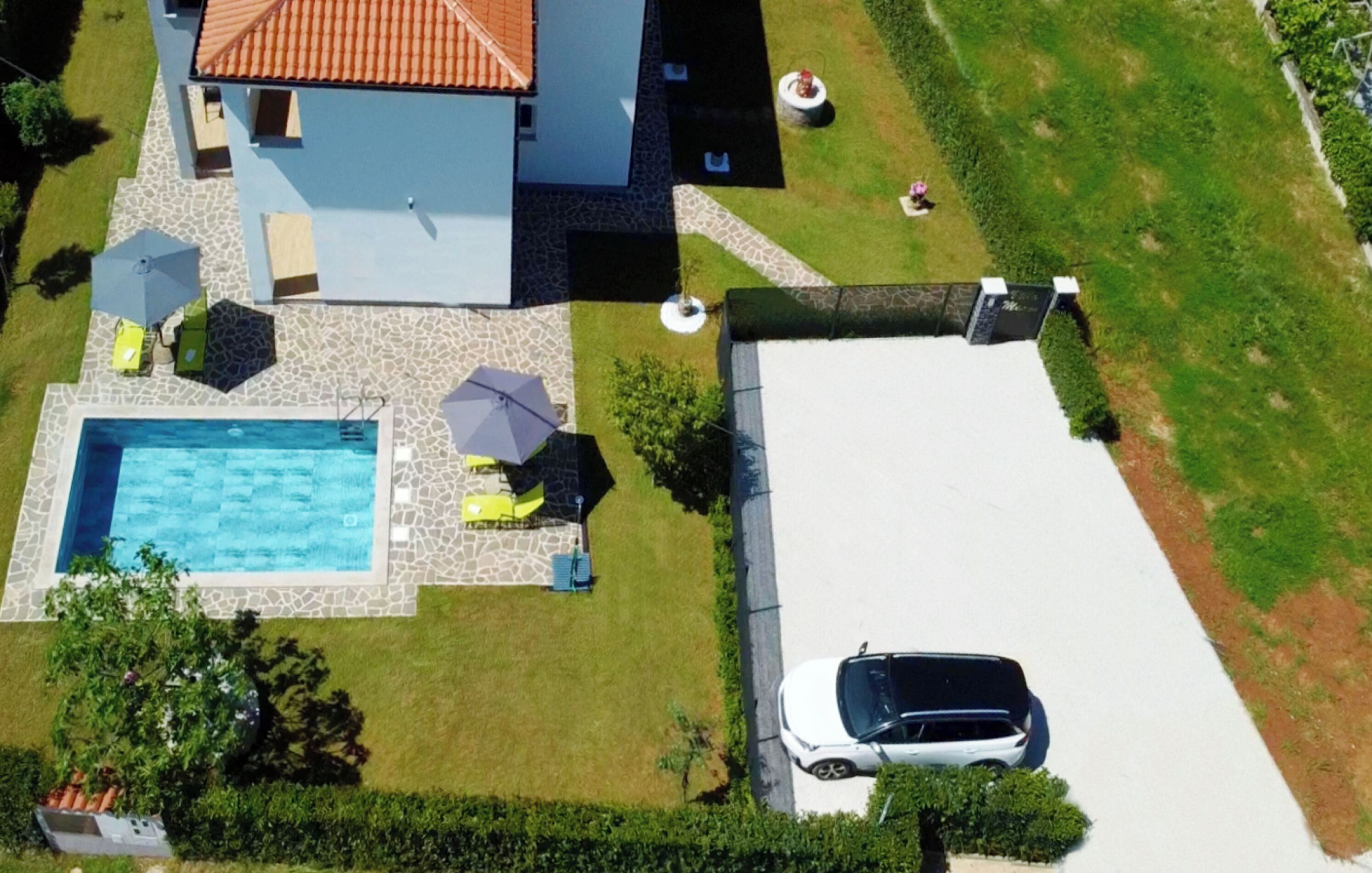 Une vue aérienne d’une maison avec une piscine, une voiture garée dans l’allée et une pelouse bien entretenue.