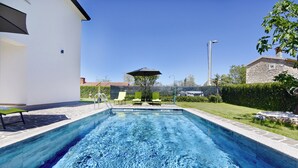 A swimming pool with lounge chairs and an umbrella, surrounded by a well-maintained lawn and a stone building. - Modern holiday home with shared pool (Čepljani)