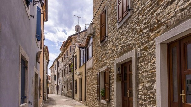 A narrow street lined with traditional stone buildings, featuring wooden doors and shutters, under a partly cloudy sky. - Modern holiday home with shared pool (Čepljani)