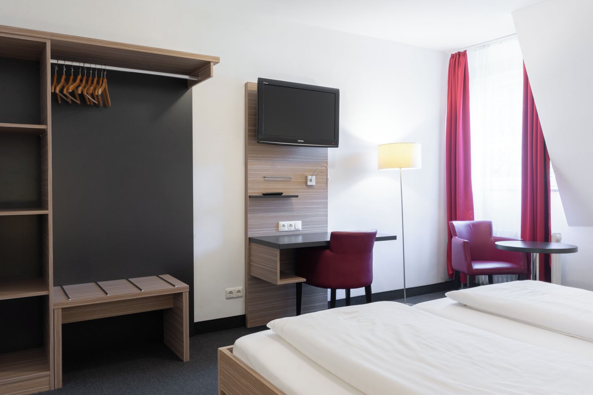 Habitación de hotel con cama, escritorio con televisor, armario y dos sillas.