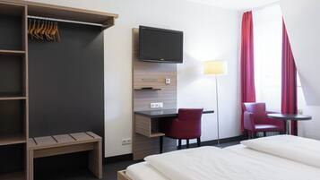 Habitación de hotel con cama, escritorio con televisor, armario y dos sillas.