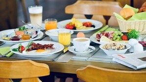 Ein Esstisch mit Tellern voller Eier, Speck, Toast und Obst, zusammen mit Kaffeetassen und Orangensaft.