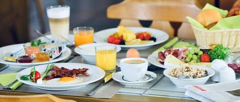 A breakfast table with plates of eggs, bacon, toast, and fruit, along with cups of coffee and orange juice.