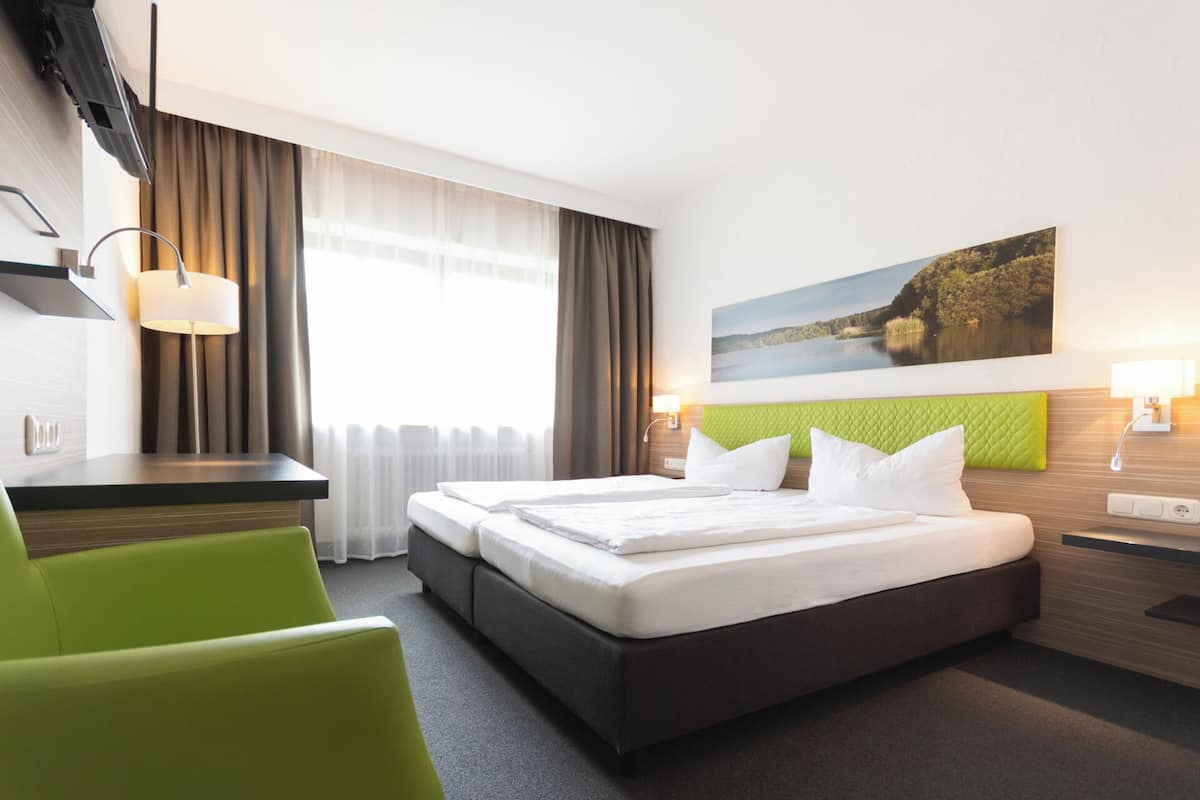 Une chambre d’hôtel avec un lit, un bureau, une chaise et un tableau au mur.