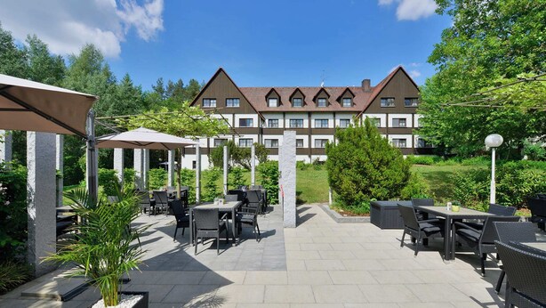 Ein Innenhof mit Außenbestuhlung, ein großes Gebäude im Hintergrund und Grünpflanzen.