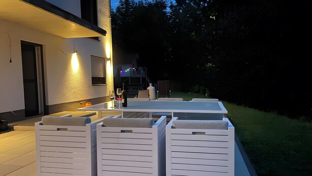 Une terrasse extérieure avec une table et des chaises, un petit coin cuisine et une vue sur une maison en arrière-plan.