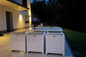 Patio esterno con tavolo e sedie, angolo cottura e vista su una casa sullo sfondo.