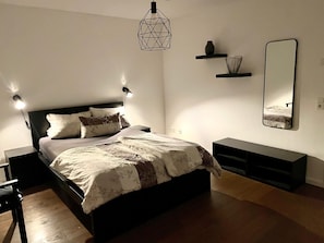 Una camera da letto con un letto, lampade da comodino, un lampadario geometrico, uno specchio e una mensola con oggetti decorativi.