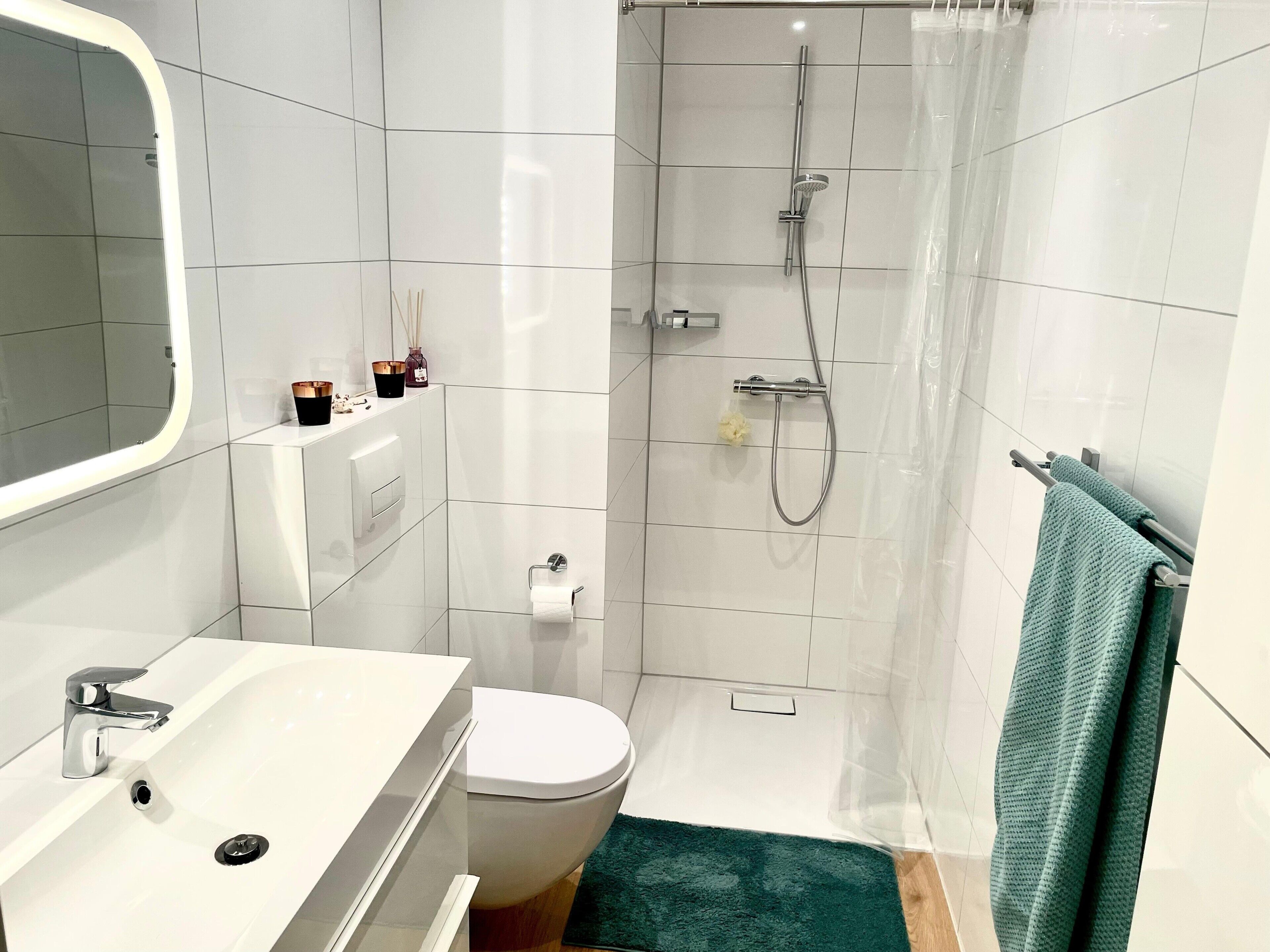 Une salle de bain moderne avec un lavabo, des toilettes et une douche, le tout de couleur blanche.
