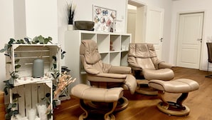 Une pièce avec deux fauteuils inclinables en cuir, une étagère blanche et un plancher en bois.