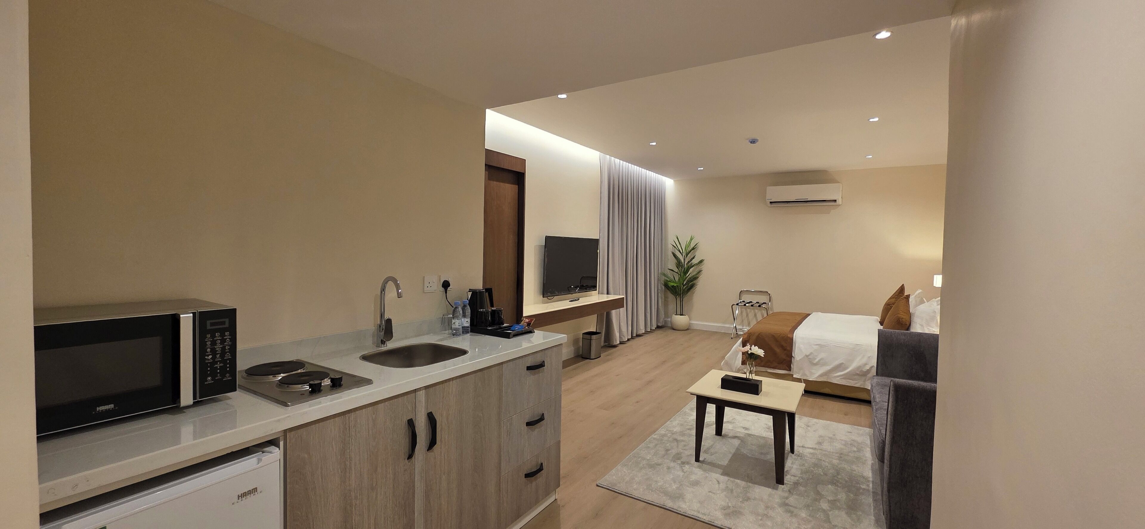 Ein modernes Hotelzimmer mit Küchenzeile, einem Bett, einem Schreibtisch und einem Fernseher.