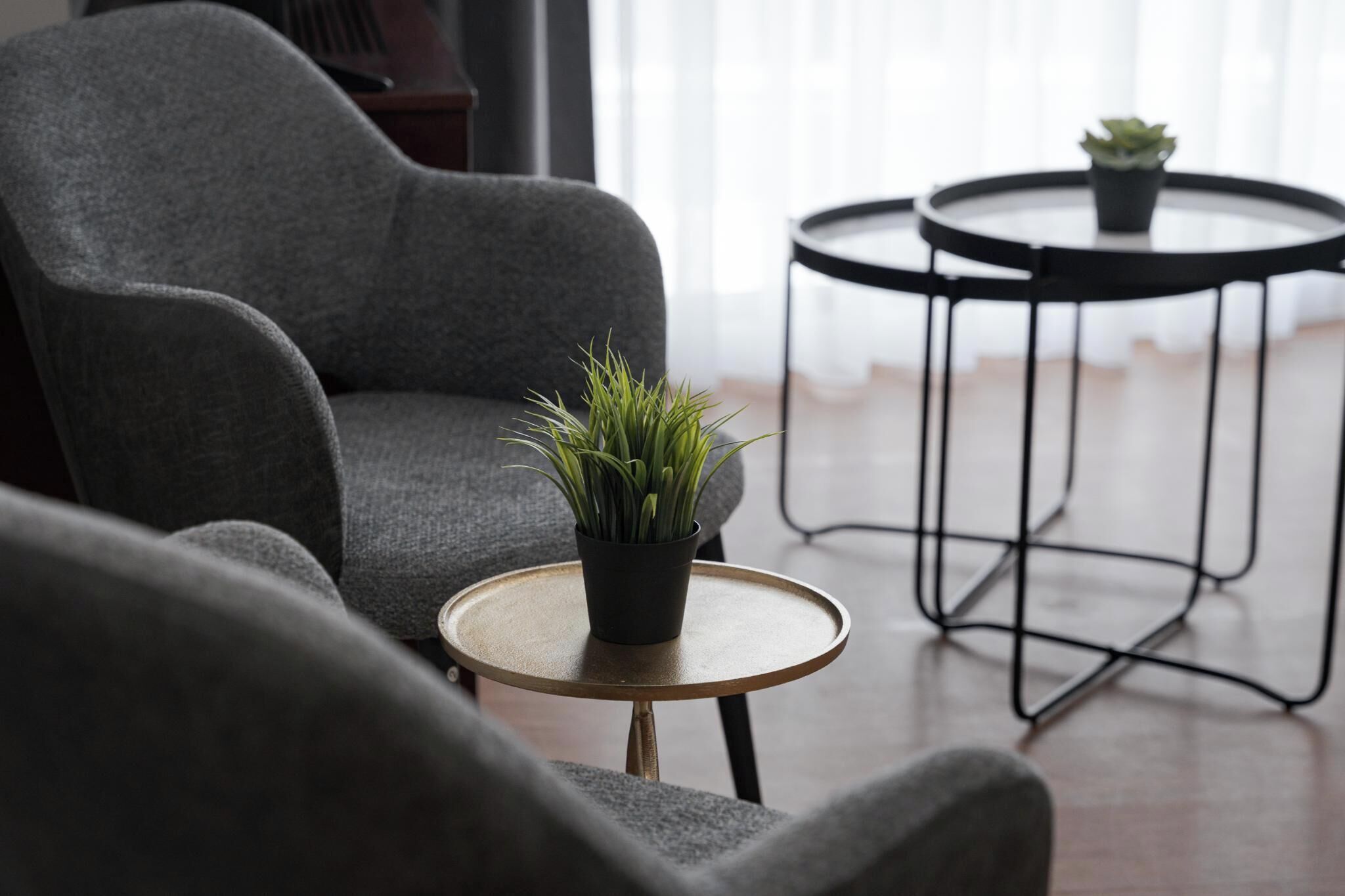 Un salon moderne avec un fauteuil gris, une petite table ronde ornée d’une plante et une autre table ronde également décorée d’une plante.