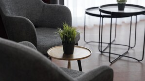 Ein modernes Wohnzimmer mit einem grauen Sessel, einem kleinen runden Tisch mit einer Pflanze und einem weiteren runden Tisch mit einer Pflanze.
