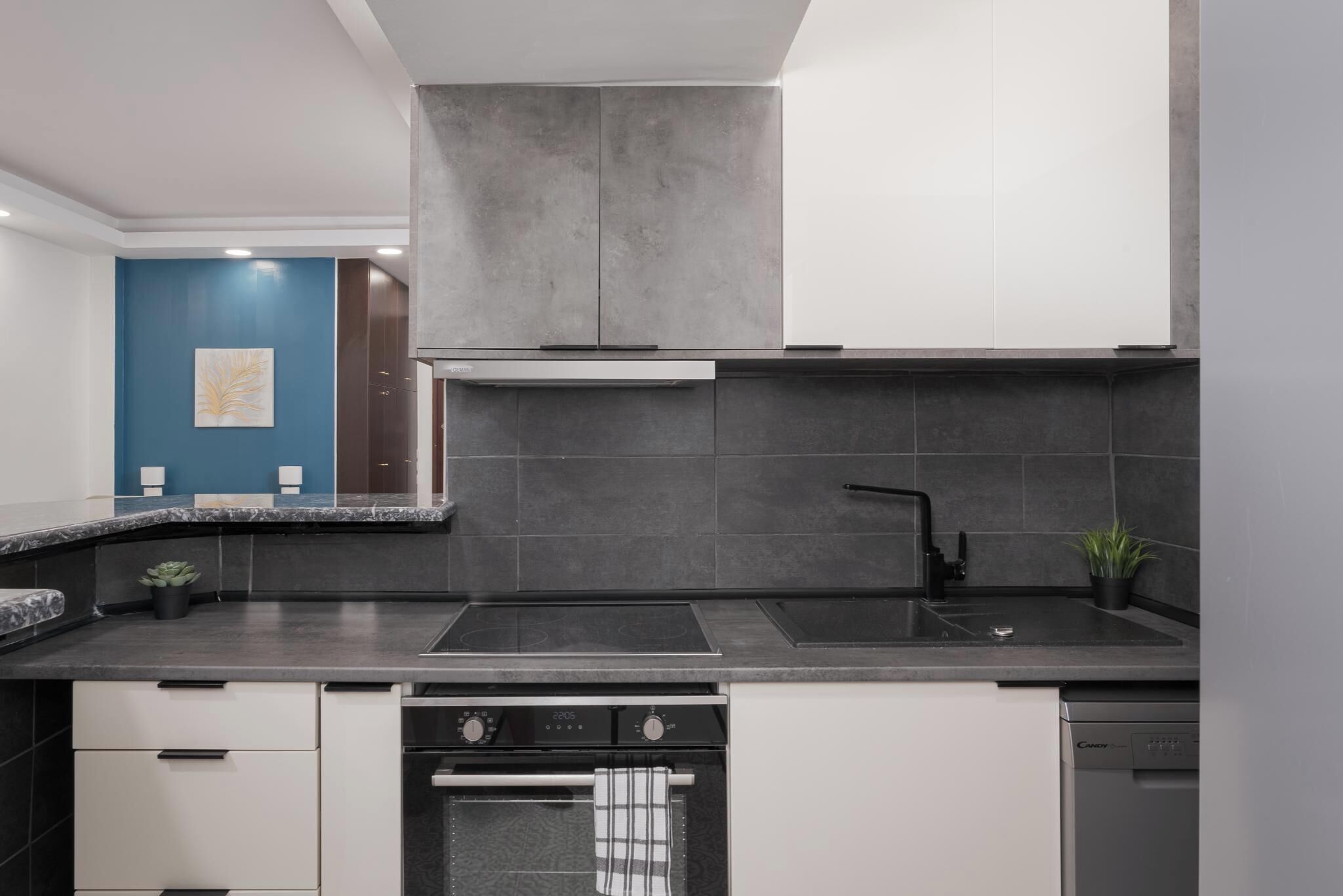 Eine moderne Küche mit schwarzem Arbeitsplatz, grauen Schränken, einem eingebauten Backofen und einer Spüle.