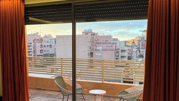 Een balkon met twee stoelen en een kleine tafel, met uitzicht op een stadslandschap met meerdere gebouwen.