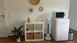 Ein Zimmer mit einem weißen Schrank, einem kleinen Heizgerät, einer Mikrowelle und einem Topf mit Pflanze.