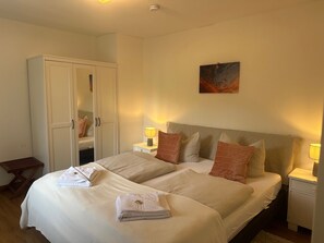 Un lit double avec deux oreillers, une table de chevet avec une lampe, une armoire et un tableau au mur.
