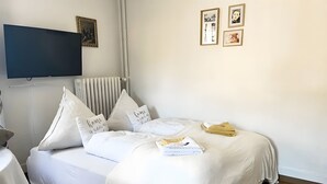 Ein ordentlich bezogenes Bett mit weißer Bettwäsche, ein an der Wand montierter Fernseher und eine Heizung.