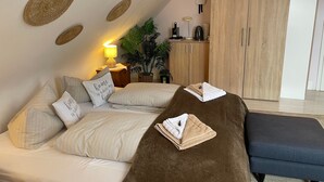 Ein gemütliches Schlafzimmer mit Bett, Nachttisch, Lampe, Topfpflanze, Kleiderschrank und einem kleinen Tisch mit Lampe.