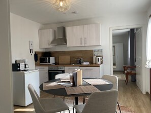 Moderni keittiö, jossa on valkoiset kaapit, mikroaaltouuni, kahvinkeitin ja ruokapöytä tuoleineen.
