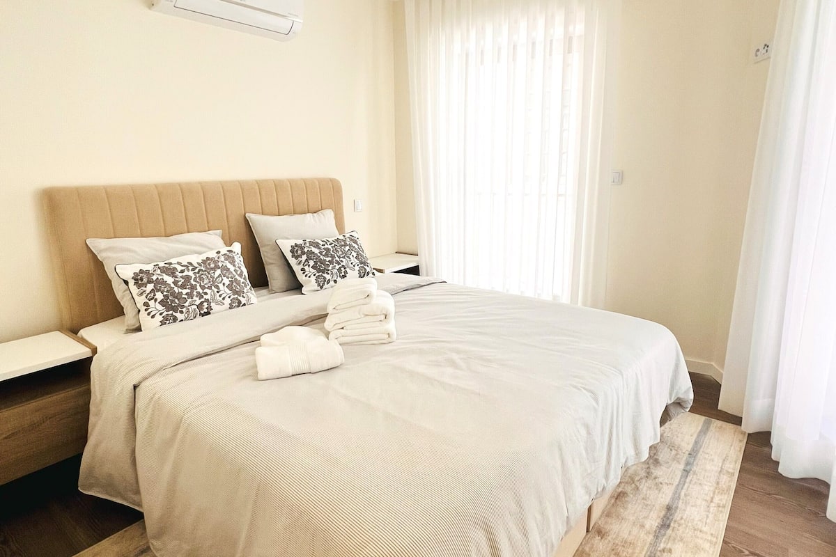 A neatly arranged bedroom with a large bed, a bedside table, and a wall-mounted air conditioner.