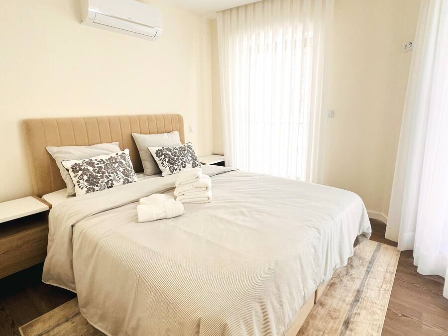 A neatly arranged bedroom with a large bed, a bedside table, and a wall-mounted air conditioner.