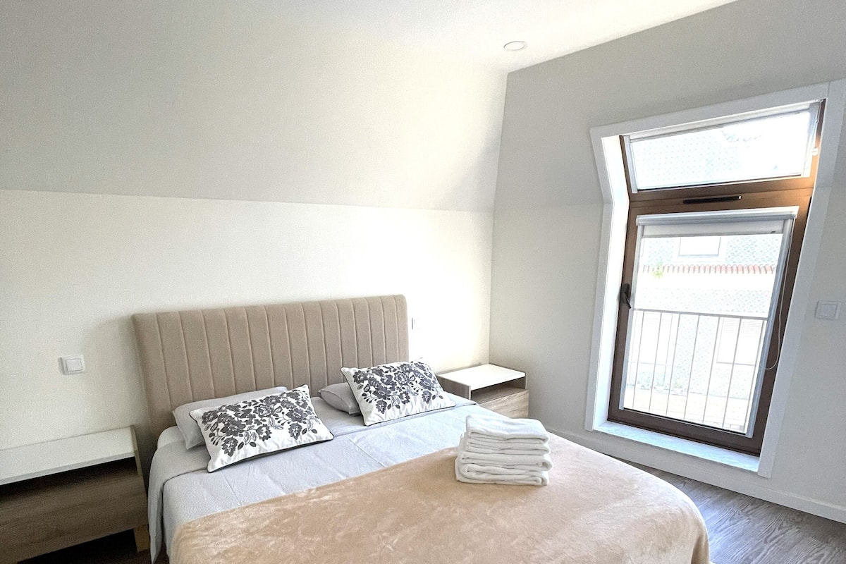 A bedroom with a bed, pillows, a bedside table, and a window.
