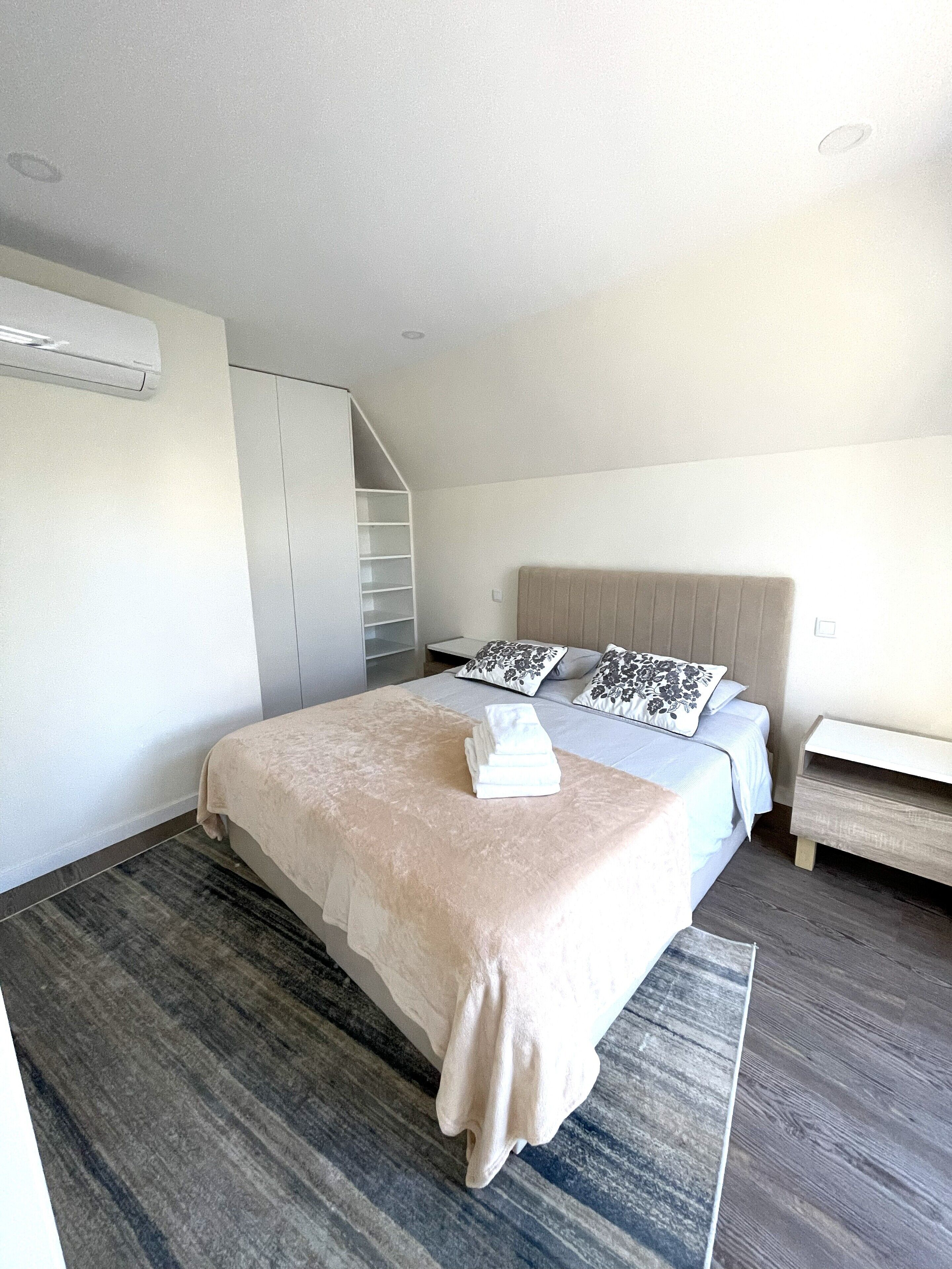 A modern bedroom with a large bed, a bedside table, a built-in wardrobe, and a staircase leading to an upper level.