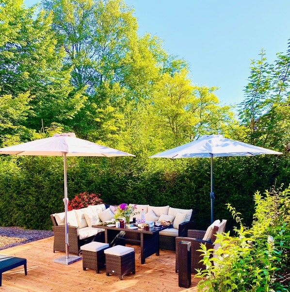 An outdoor patio with wicker furniture, two umbrellas, and a table with various items.
