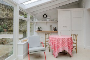 A conservatory with a table and chairs, a bench, and a shelf with decorative items. - Secret Garden Square, by Veeve (London)
