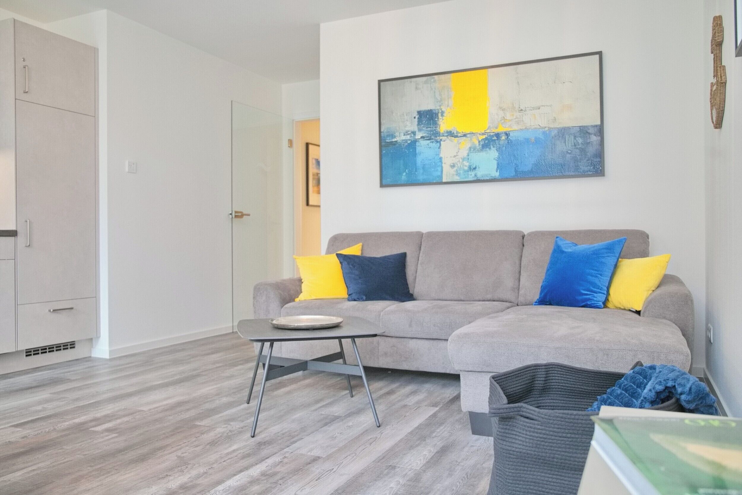 Un salon moderne avec un canapé gris, une petite table et un tableau accroché au mur.