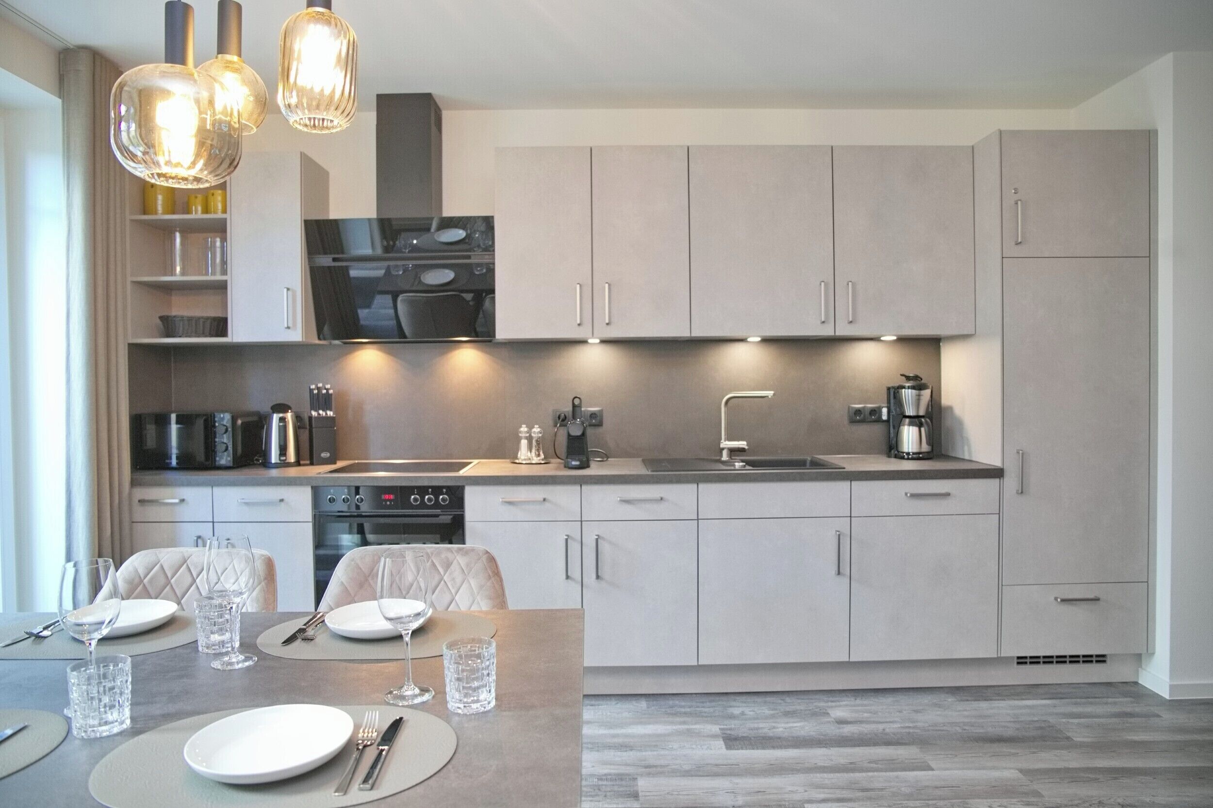 Uma cozinha moderna com eletrodomésticos embutidos, sala de jantar com mesa posta para dois e iluminação pendente.