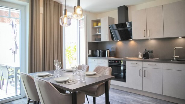 Una cucina moderna con zona pranzo, che presenta un tavolo apparecchiato per due, un forno integrato e un'ampia finestra con tende.