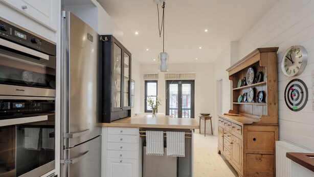 A modern kitchen with stainless steel appliances, a wooden island, and a vintage clock. - South Kensington Mews Hideaway, by Veeve (London)