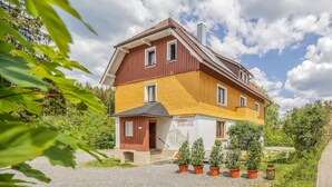 A two-story house with a yellow and red exterior, a small porch, and potted plants in front. - 'Sandvoss' 3-Room Apartment by Gästehaus Sandvoss, Near Lake, Titisee (Titisee-Neustadt)