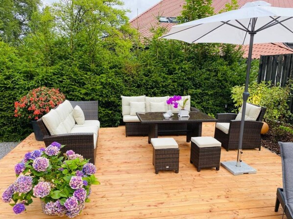 Une terrasse extérieure aménagée avec des meubles en osier, une table et un grand parasol.