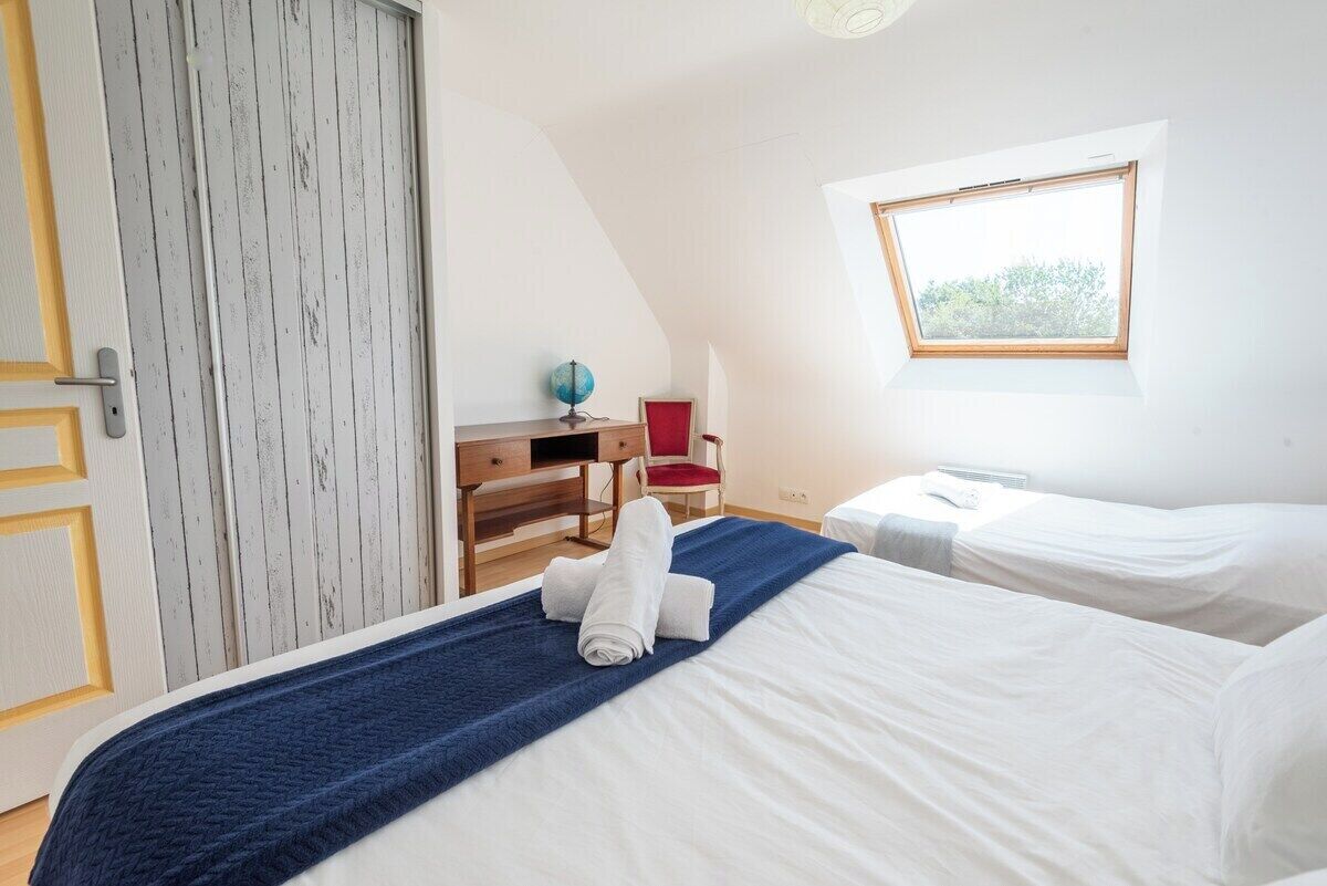 A bedroom with two beds, a desk, a chair, a globe, and a window.