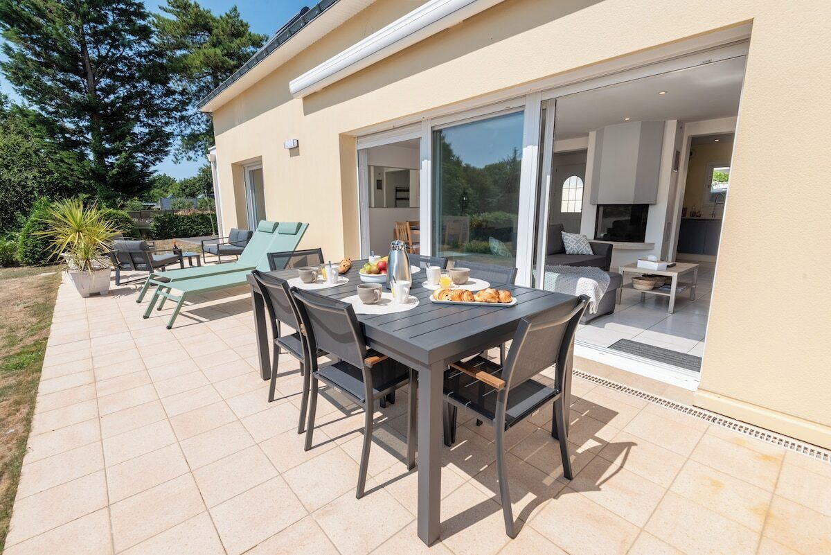An outdoor dining area with a table and chairs, a potted plant, and a sliding glass door leading to an interior space.