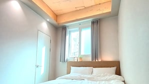 Un dormitorio con techo de madera, una cama, una ventana con cortinas y una puerta.