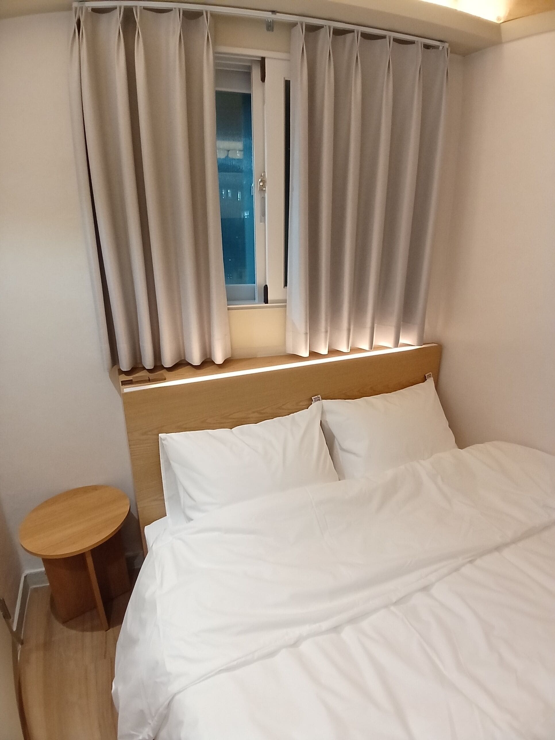 Une chambre d’hôtel avec un lit, une petite table en bois, une fenêtre avec des rideaux et une vue sur l’extérieur.